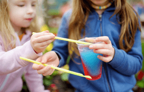 Two cute little sisters drinking colorful frozen slushie drink on hot summer day