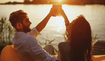 Young happy couple enjoy in beer by the river during the sunset
