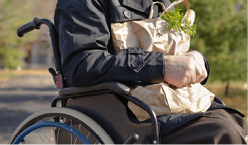 Clouse up Senior handicapped man doing his grocery shopping sitting in the road in his wheelchair clutching a large bag of food and looking at the camera
