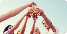 summer, holidays, tourism, drinks and people concept - group of smiling friends clinking bottles of beer or cider on beach