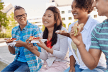 people, friendship and international concept - group of happy friends eating sandwiches or burgers in park