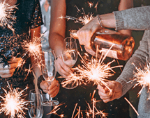 Friends celebrating Christmas or New Year eve party with Bengal lights and rose champagne.
