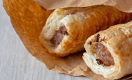 Sausage rolls in a brown paper bag, environmentally friendly biodegradable packaging, with a grey wood background
