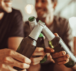Close up of three friends toasting their bottles of beer while having a party at home. Men raising their bottles for a toast sitting at home.