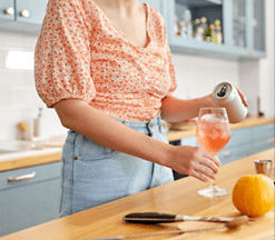 drinks and people concept - close up of woman pouring soda from tin can to wine glass and making orange cocktail at home kitchen