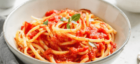 Traditional pasta with tomato and Greek basil sauce in a ceramic bowl on a white table. 