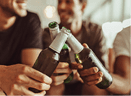 Close up of three friends toasting their bottles of beer while having a party at home. Men raising their bottles for a toast sitting at home.