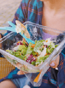 A happy girl is snacking on a ready-to-eat salad in a city park. Diet and cheap takeaway fast food on the street